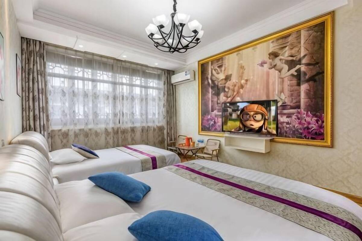 Ένα δωμάτιο ξενοδοχείου με δύο κρεβάτια, ένα πολυέλαιο, έναν πίνακα και μια τηλεόραση.