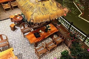 A dining area with a thatched roof, wooden furniture, and a view of a water body. - kong shan niao yumin su (Ya'an)