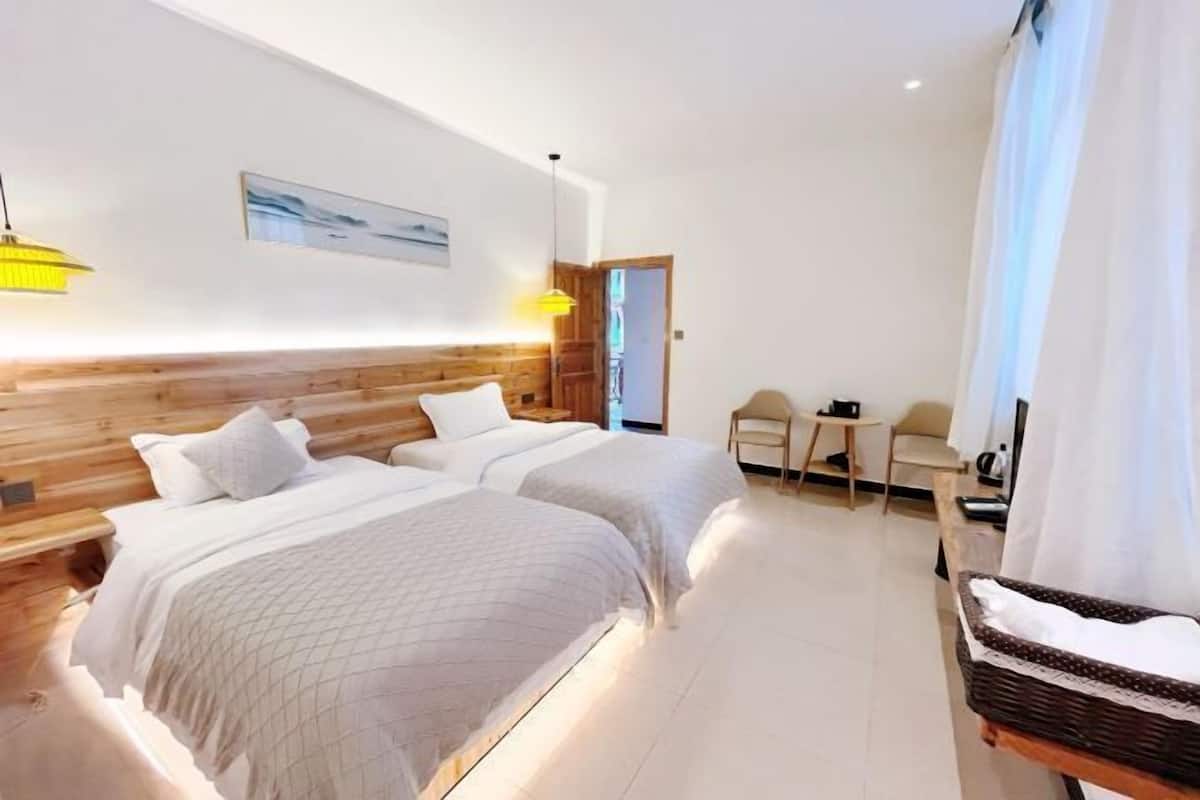 Een hotelkamer met twee bedden, een houten hoofdeinde, een kleine tafel, een stoel en een rieten mand.