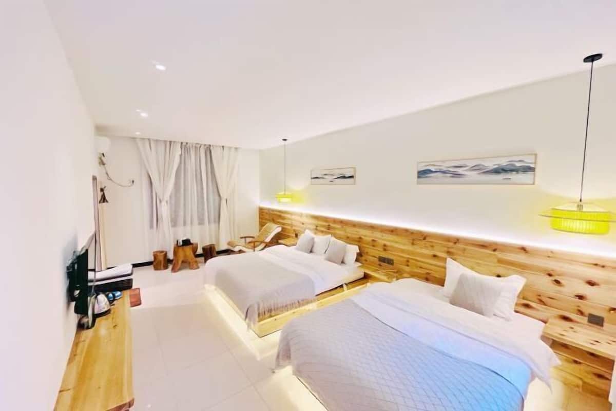 Een hotelkamer met twee bedden, een houten hoofdbord, een bureau, een stoel, een lamp en een schilderij aan de muur.