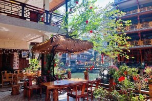 Un espace de restauration intérieur aménagé avec du mobilier en bois, doté d’un toit de chaume et offrant une vue sur l’architecture traditionnelle.