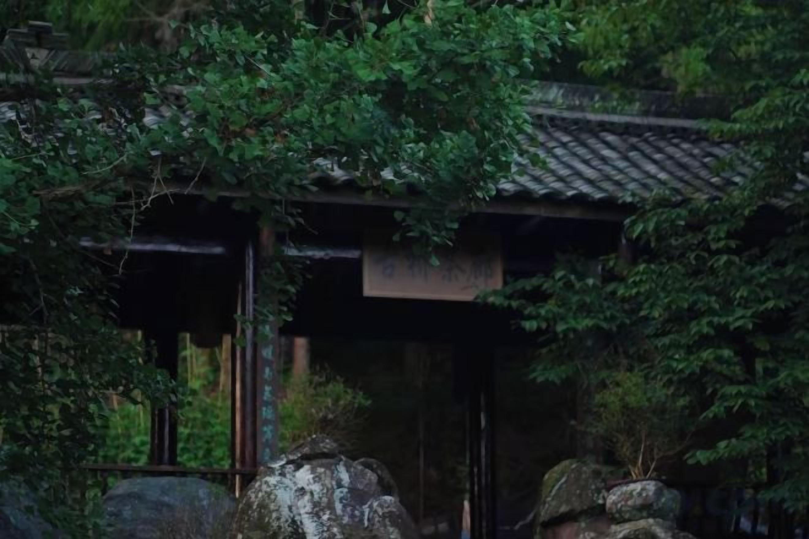 A traditional Japanese building with a tiled roof, surrounded by dense foliage.
