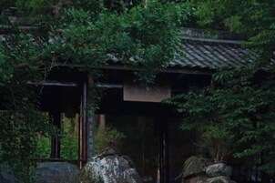 A traditional Japanese building with a tiled roof, surrounded by dense foliage.