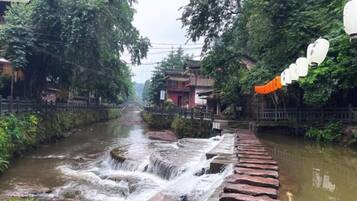 Un río con una pequeña cascada, rodeado de vegetación y edificios.