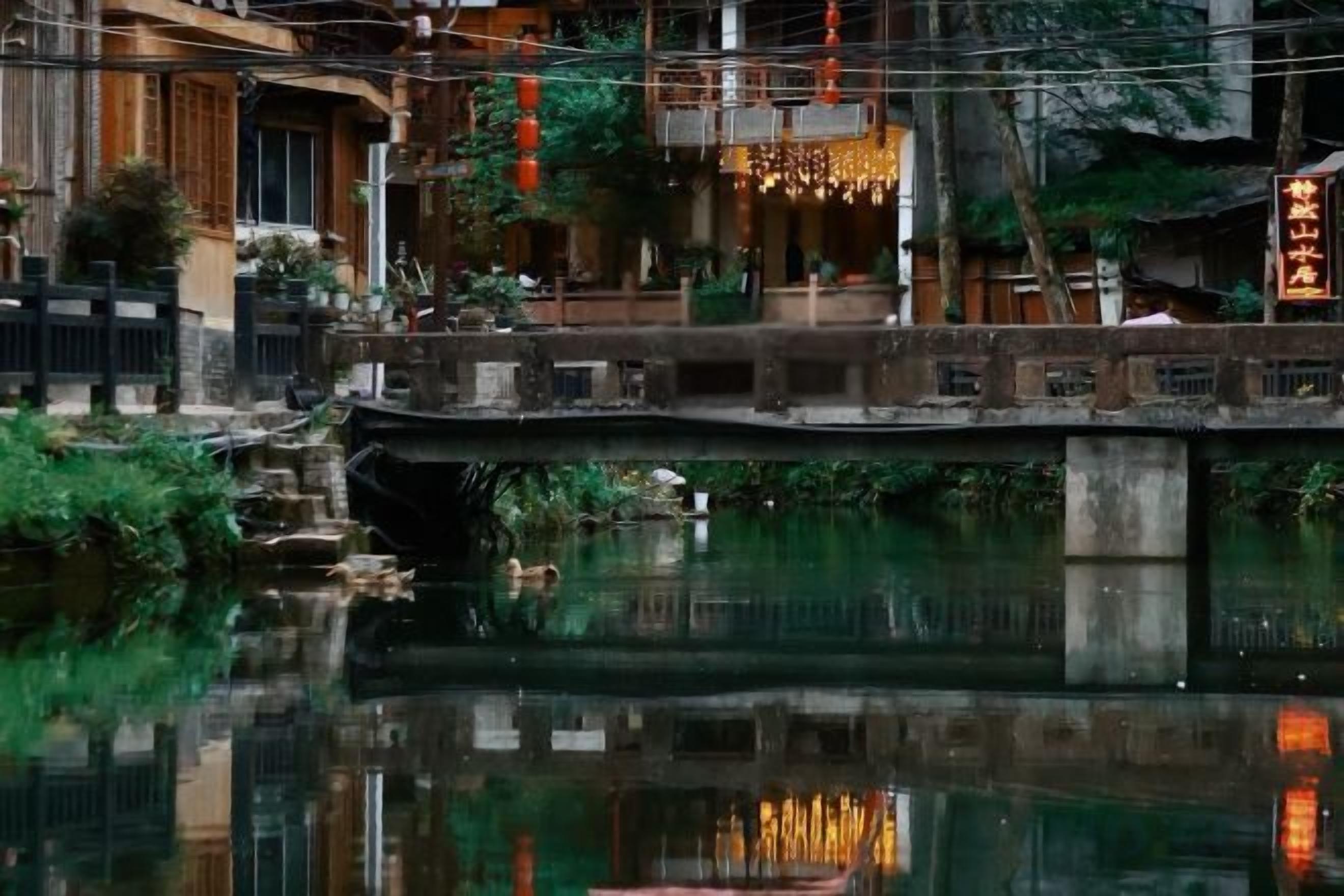 Un puente tradicional sobre aguas tranquilas, reflejando edificios y vegetación cercanos.