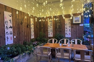 A wooden interior with a dining table and chairs, surrounded by plants and hanging lights.