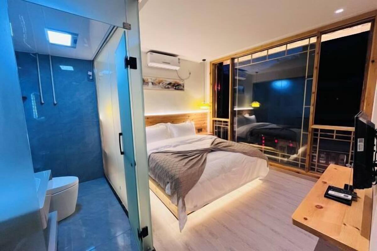 Een moderne hotelkamer met een bed, nachtkastje en een schuifdeur naar een balkon.