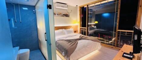Una habitación de hotel moderna con cama, mesita de noche y puerta corredera que da a un balcón.