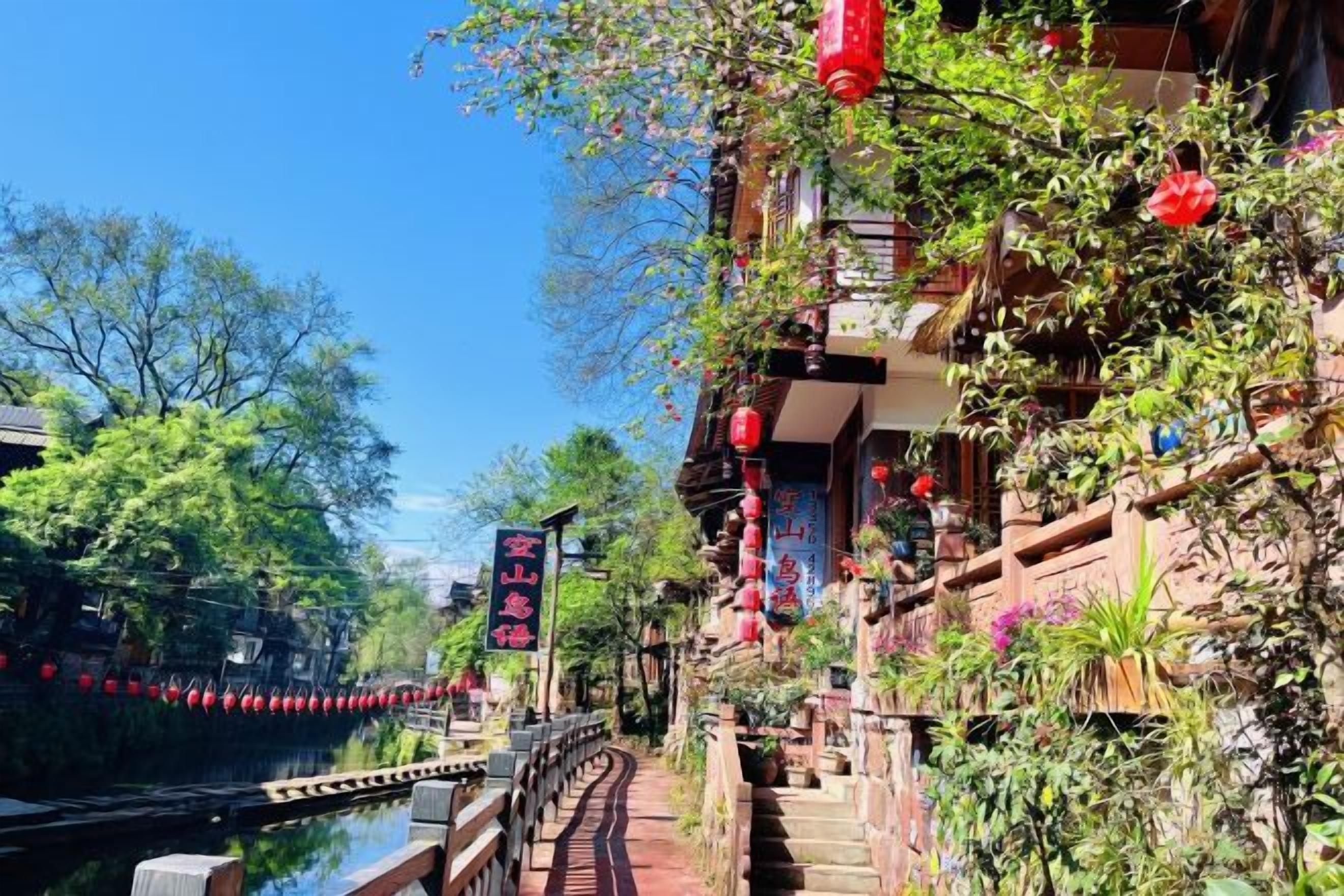 A traditional Chinese courtyard with a waterway, wooden bridge, and red lanterns.