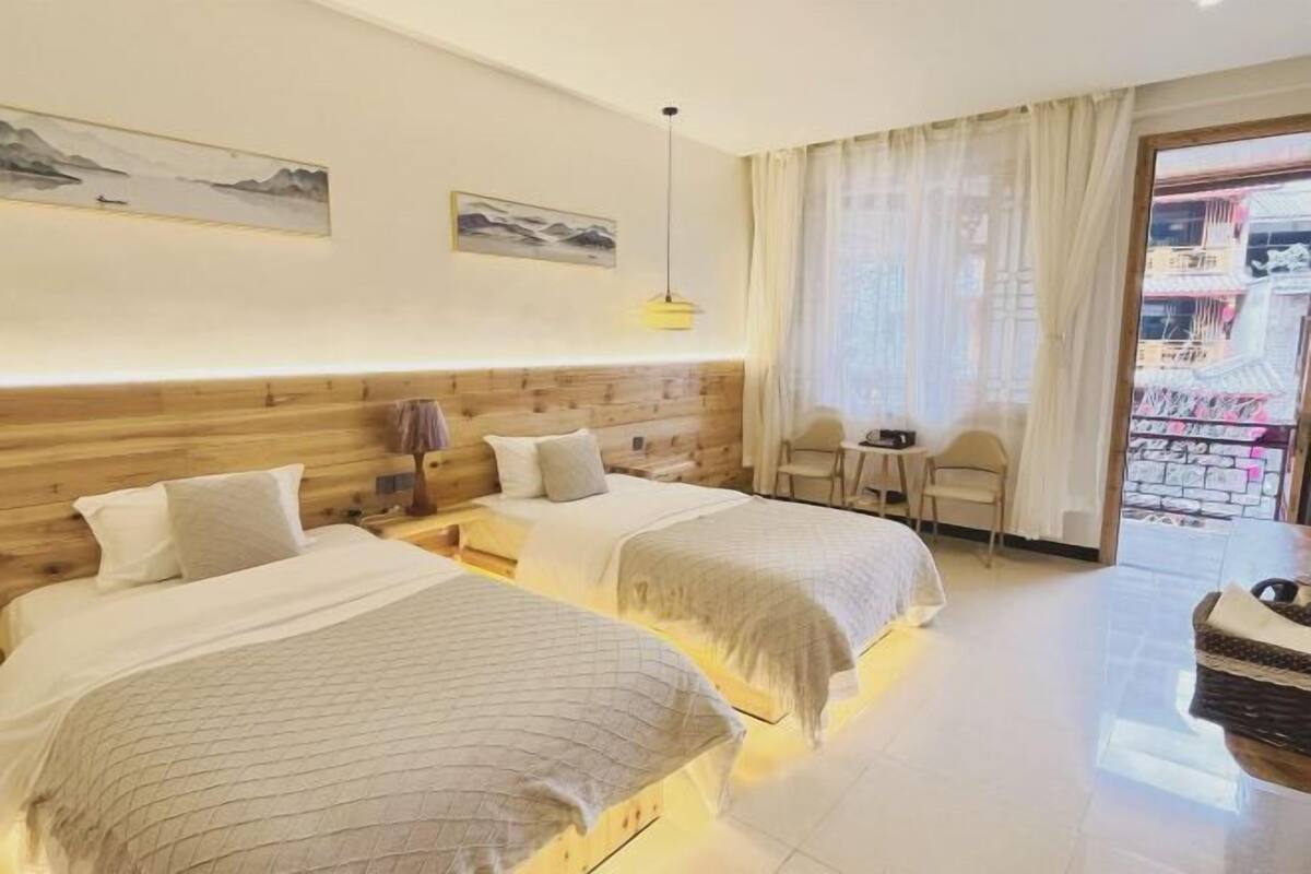 Een hotelkamer met twee bedden, een houten hoofdeinde, een tafeltje, een stoel en een balkon met uitzicht.