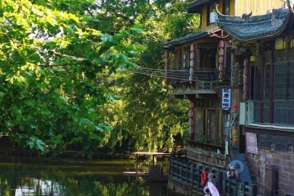 A traditional building with a balcony overlooking a calm water body, surrounded by lush greenery.