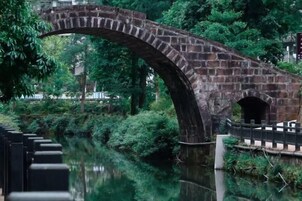 A stone bridge over a calm river, surrounded by lush greenery.