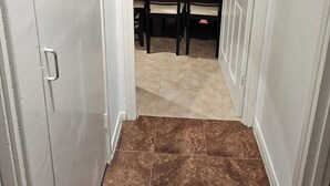 A hallway with a dining area featuring a table and chairs, a clock on the wall, and a door with a handle. - Mitcham Junction - 2 Bed Apartment - Sleeps 6 (London)
