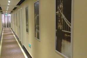 Een hotelgang met een lange hal, posters aan de muur en uitzicht op een brug.