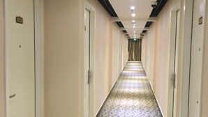 A hotel corridor with patterned carpet, white walls, and doors on both sides.