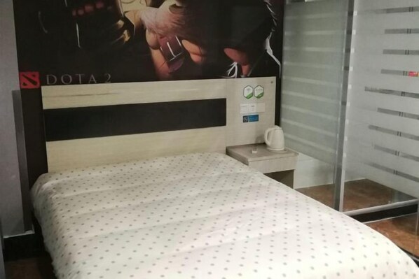 Un lit recouvert d’une couvre-lit à pois blancs, une table de chevet avec une lampe blanche et un mur orné d’une affiche.