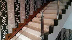 A staircase with a wooden handrail and glass railings, leading to a landing with a patterned wall.