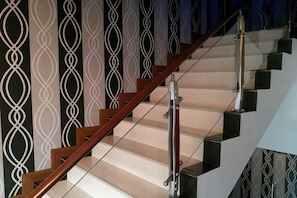 Een trap met een houten leuning en glazen balustrades, leidend naar een plateau met een patroon in de muur.