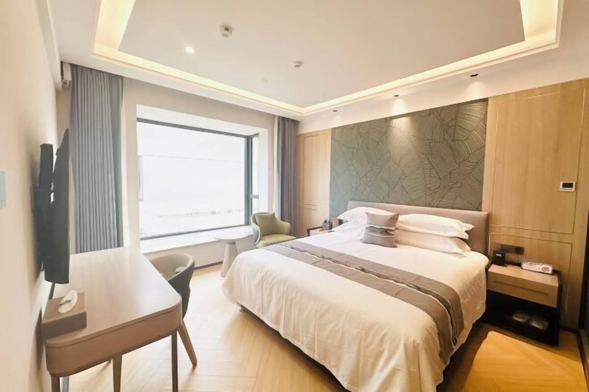 A modern hotel room with a large bed, a desk, a chair, and a TV.