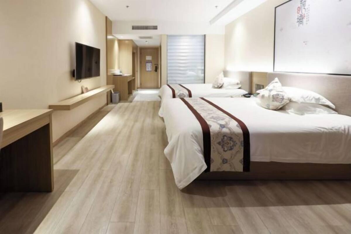 A hotel room with two beds, a TV, a desk, and a bathroom.
