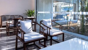 A modern lounge area with glass walls, wooden chairs with white cushions, and a marble table. - Yangzi Hotel (Nanjing)