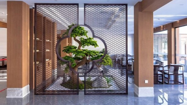 A modern indoor space with a decorative tree in a glass enclosure, wooden paneling, and a seating area with tables and chairs. - Yangzi Hotel (Nanjing)
