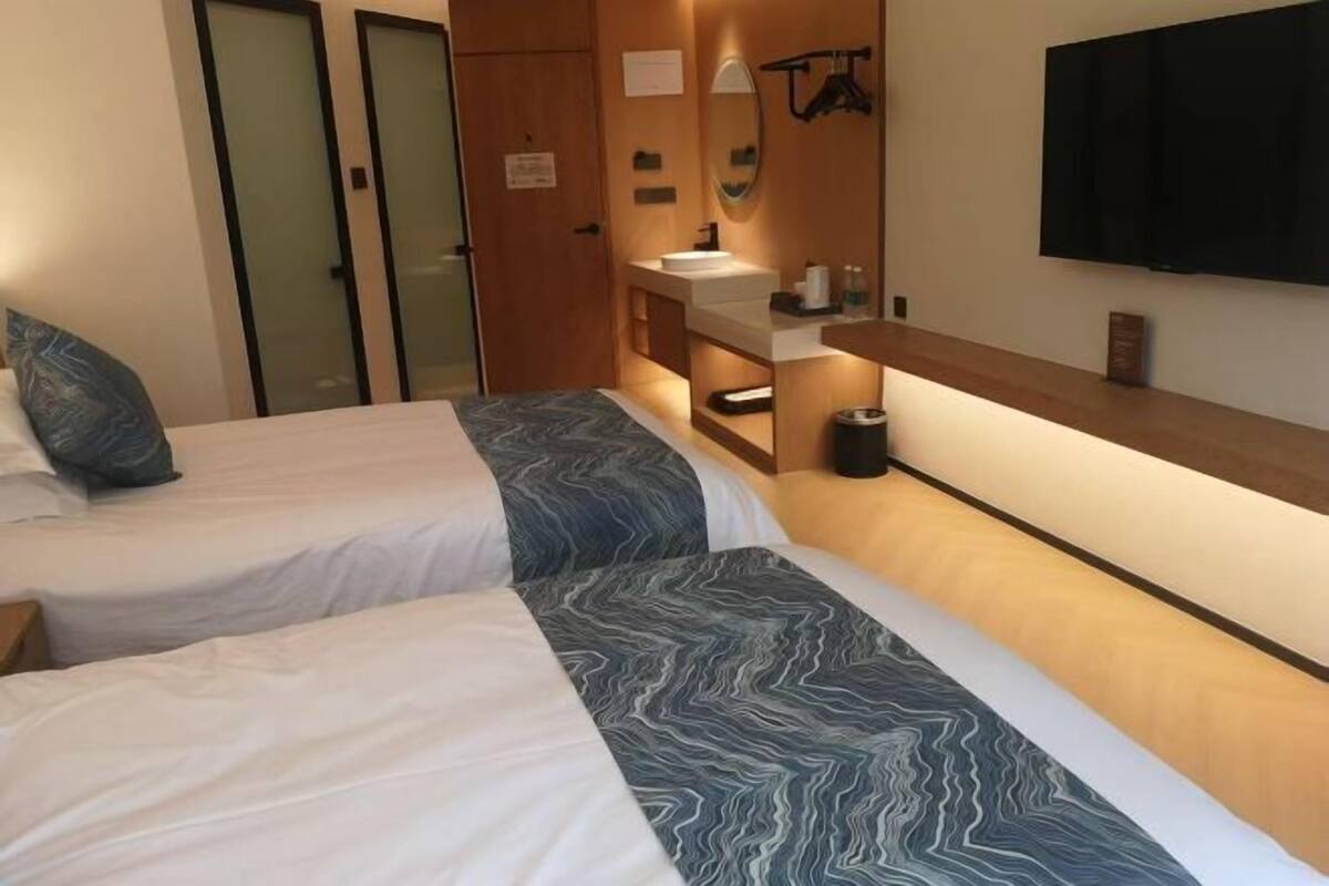 A hotel room with two beds, a bathroom, a TV, and a wooden shelf.