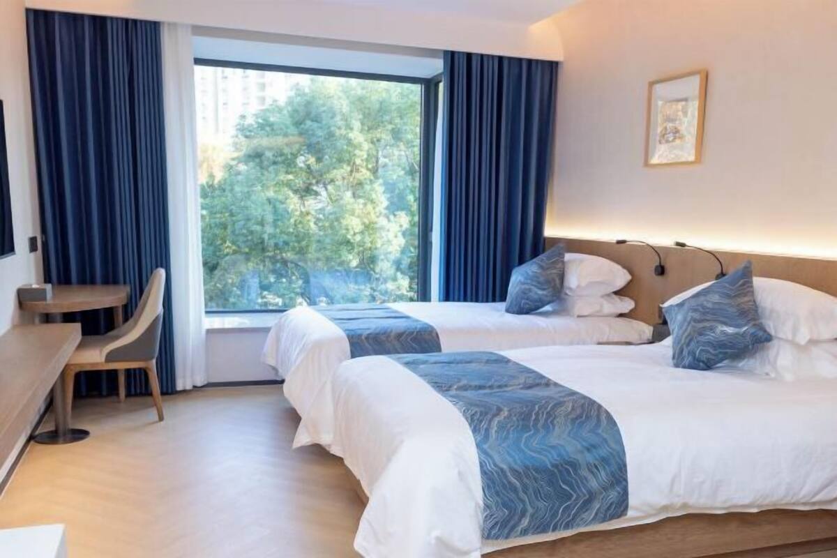 A hotel room with two beds, a desk, and a large window with curtains.