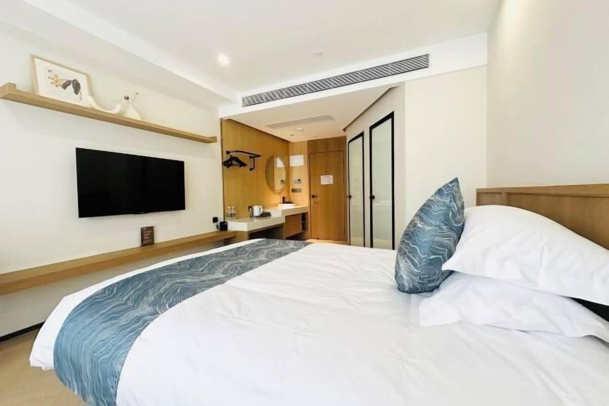 A hotel room with a bed, a TV, a mirror, a wooden cabinet, and a door.