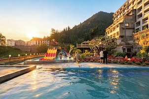 Una piscina con tobogán y puente, rodeada de un jardín ajardinado y un edificio.
