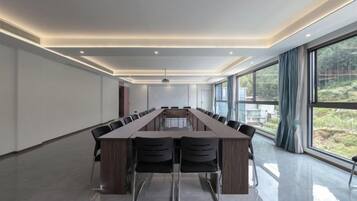 A conference room with a long table, chairs, and a view through large windows.