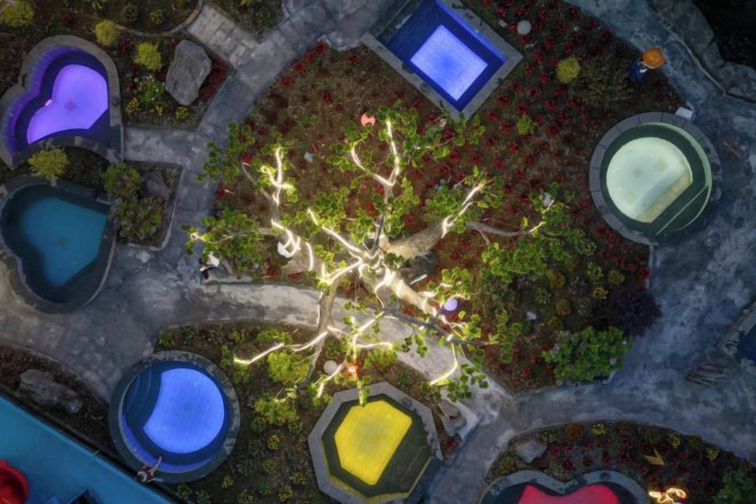 An aerial view of a landscaped area with multiple water features, including pools and fountains, arranged around a central tree.