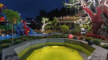 A water feature with a pool, surrounded by a playground with slides and a climbing structure, and a decorative tree with lights.