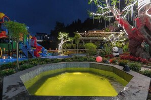 A water feature with a pool, surrounded by a playground with slides and a climbing structure, and a decorative tree with lights.