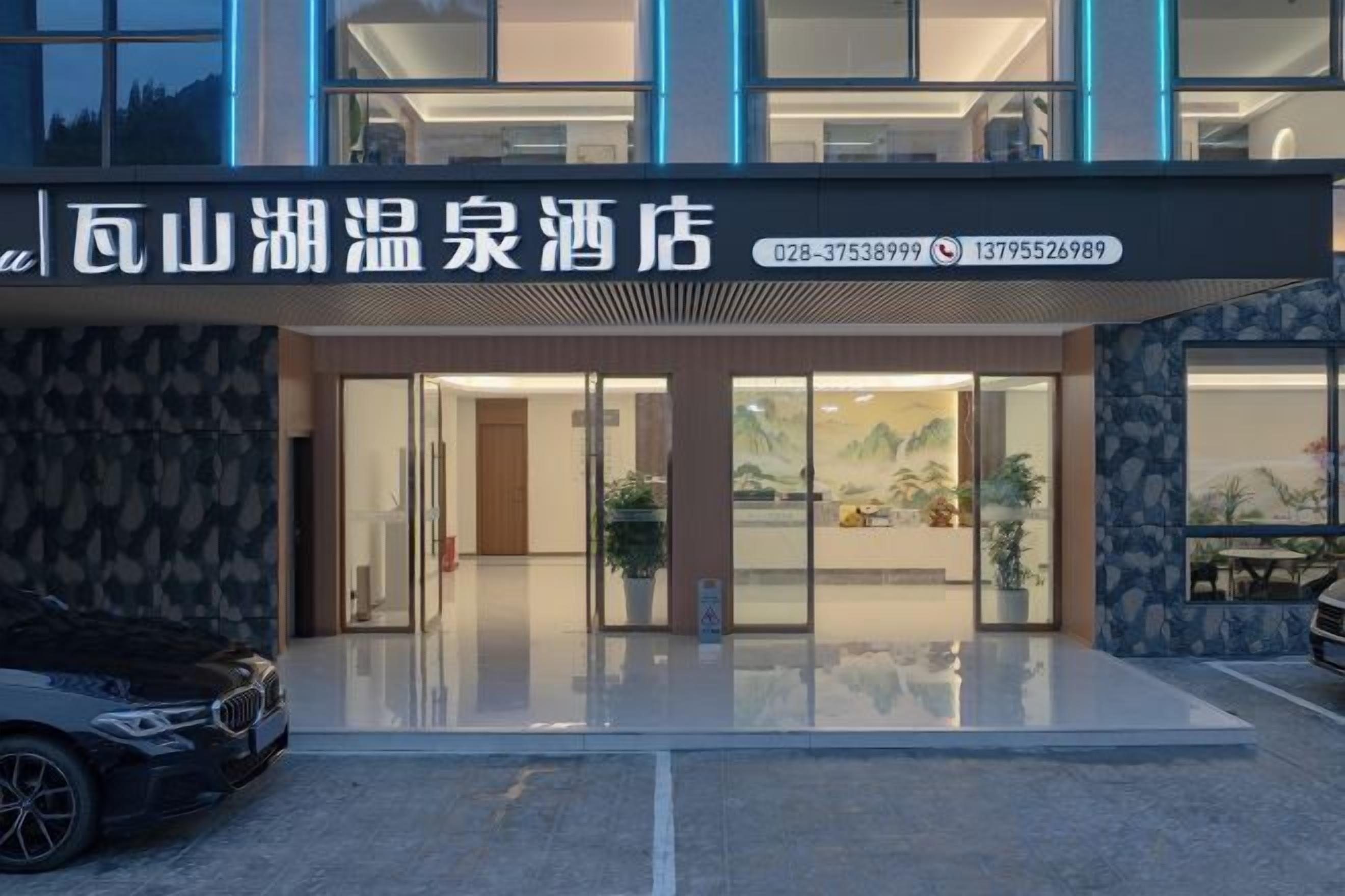 A hotel entrance with a modern design, glass doors, and a parking area in front.