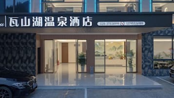A hotel entrance with a modern design, glass doors, and a parking area in front.