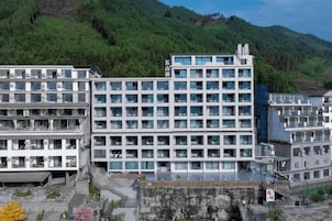 Un hotel de varios pisos con un diseño moderno, que cuenta con un patio central y un telón de fondo de montañas.