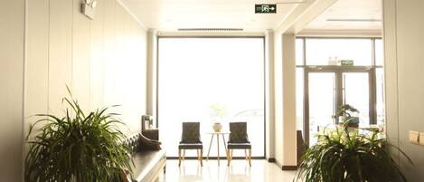 A hotel lobby with a reception desk, two chairs, and potted plants.