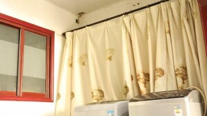 Une pièce équipée de deux climatiseurs, avec une fenêtre à cadre rouge et un rideau orné d’un motif de coquillages.