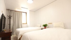 Une chambre d’hôtel avec deux lits, un bureau, un miroir, une plante en pot et une fenêtre avec des rideaux.
