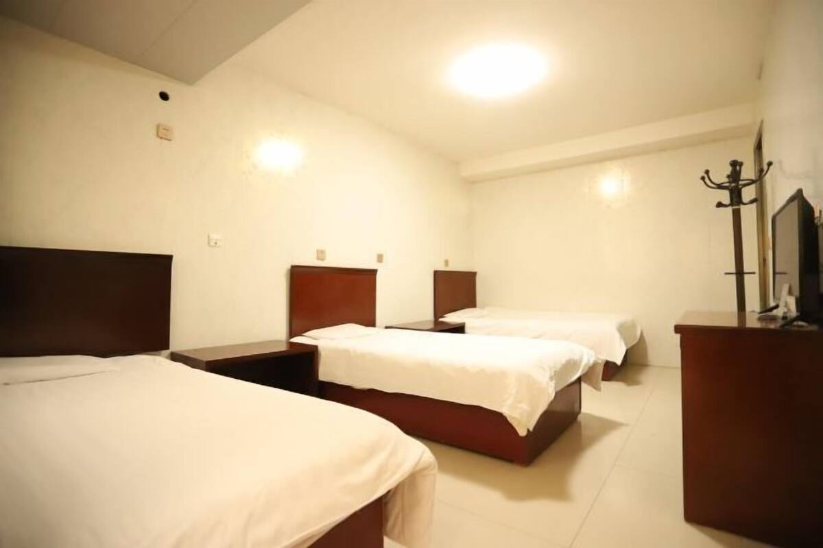 Een hotelkamer met drie bedden, een houten hoofdeinde, een bureau en een spiegel.