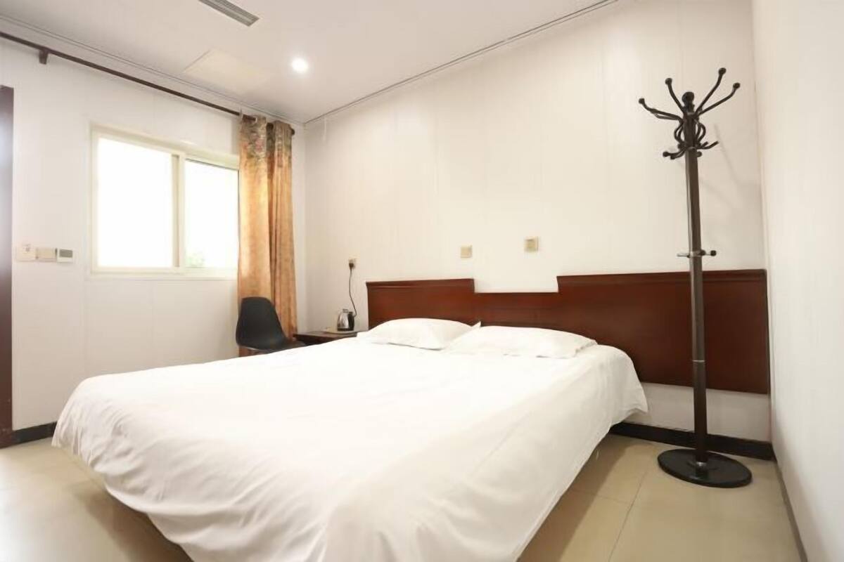 Een hotelkamer met een bed, een stoel, een kapstok en een raam met gordijnen.
