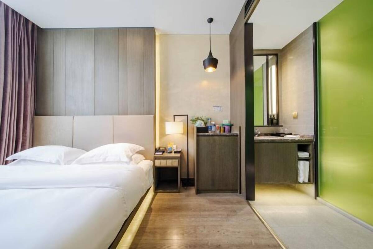 Une chambre d’hôtel comprenant un lit, une table de chevet, une lampe et une petite salle de bain avec un miroir et un lavabo.