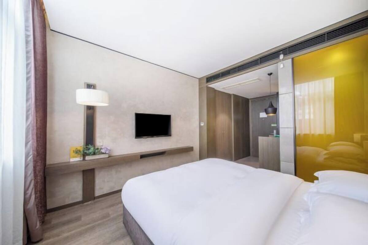 Une chambre d’hôtel avec un lit, un téléviseur à écran plat fixé au mur, une table de chevet avec une lampe et un miroir qui reflète une partie de la pièce.