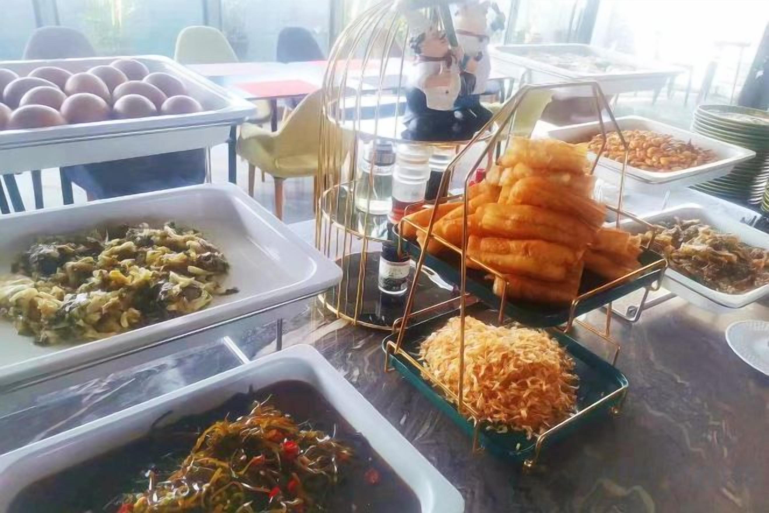 A buffet table with various food items including a tray of eggs, a dish of greens, and a container of shredded cheese.