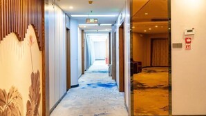 A hotel corridor with a wooden panel wall on the left, a carpeted floor, and a door leading to a room on the right. - Kunxing Century Hotel (Lotus Plaza) (Lianhua)