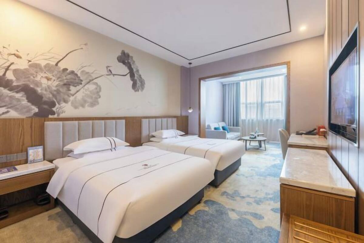 Habitació d'hotel amb dos llits, una taula de treball, una televisió, un finestral gran i un mural a la paret.