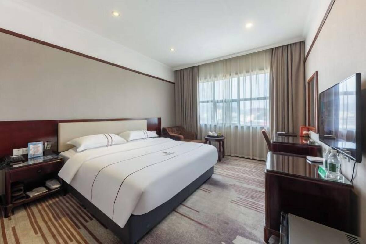 Habitació d'hotel amb un llit gran, una taula de treball amb una cadira, televisió i una finestra amb cortines.