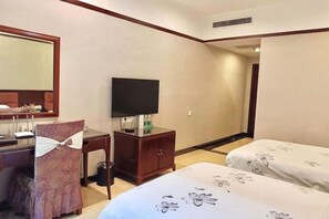 A hotel room with a bed, a desk with a TV, a chair with a bow, and a small cabinet.