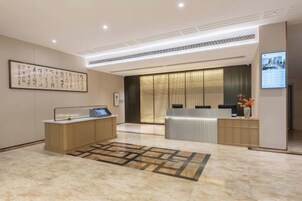 Un moderno vestíbulo de hotel con mostrador de recepción, una pantalla digital y una celosía decorativa tradicional.